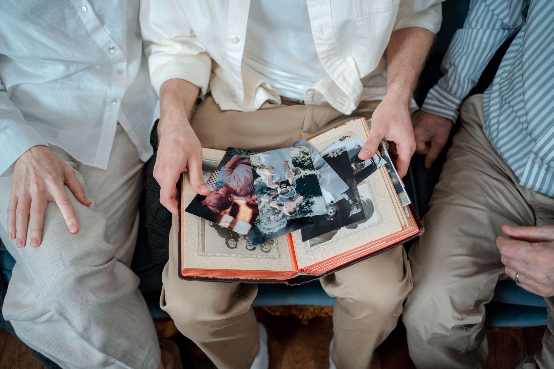 Trzej mężczyźni w białych i błękitnych koszulach przglądają starą rodzinną fotografię w otwartym albumie.