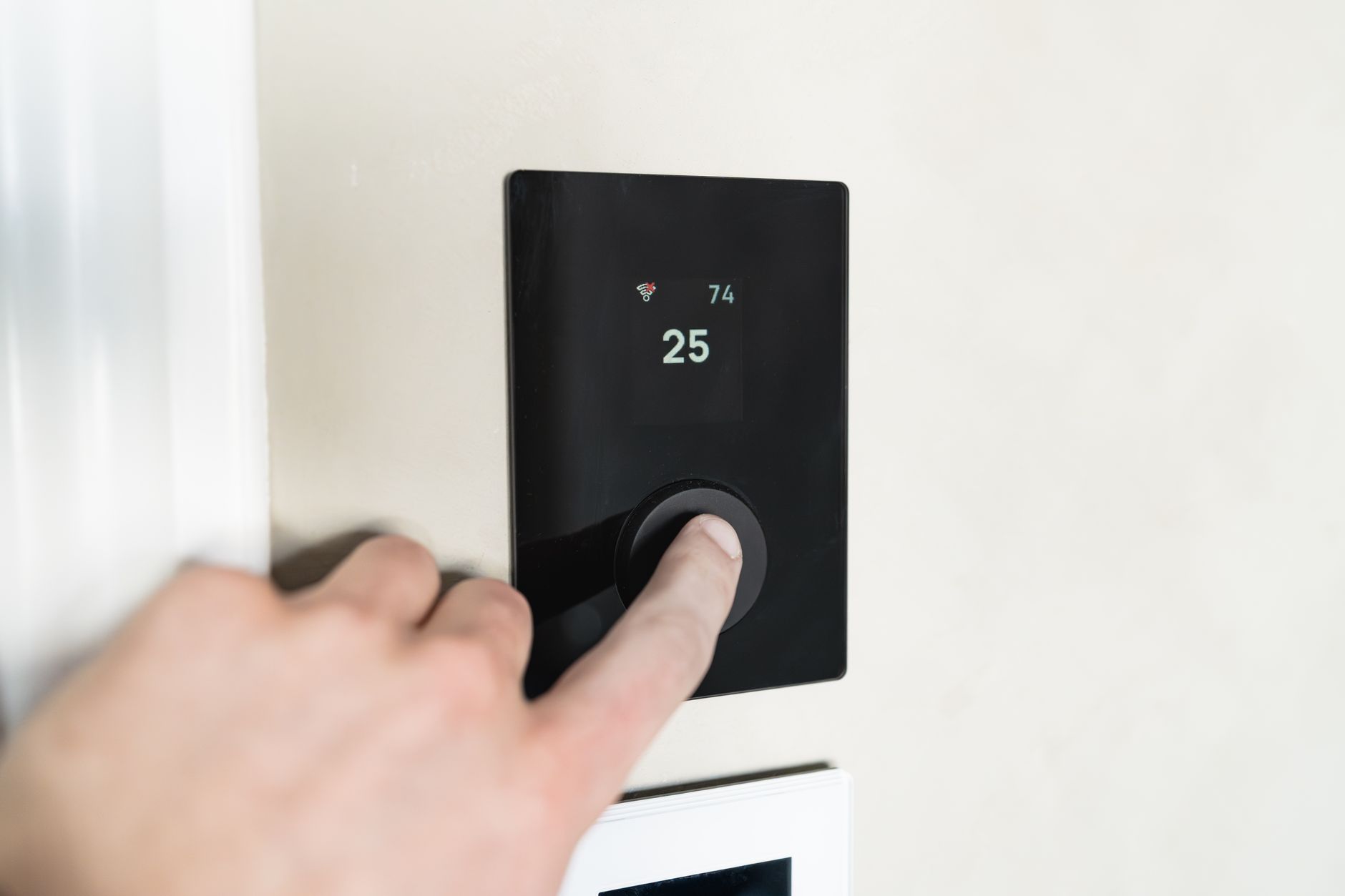 Palec osoby naciska przycisk na cyfrowym termostacie pokazującym temperaturę 25°C