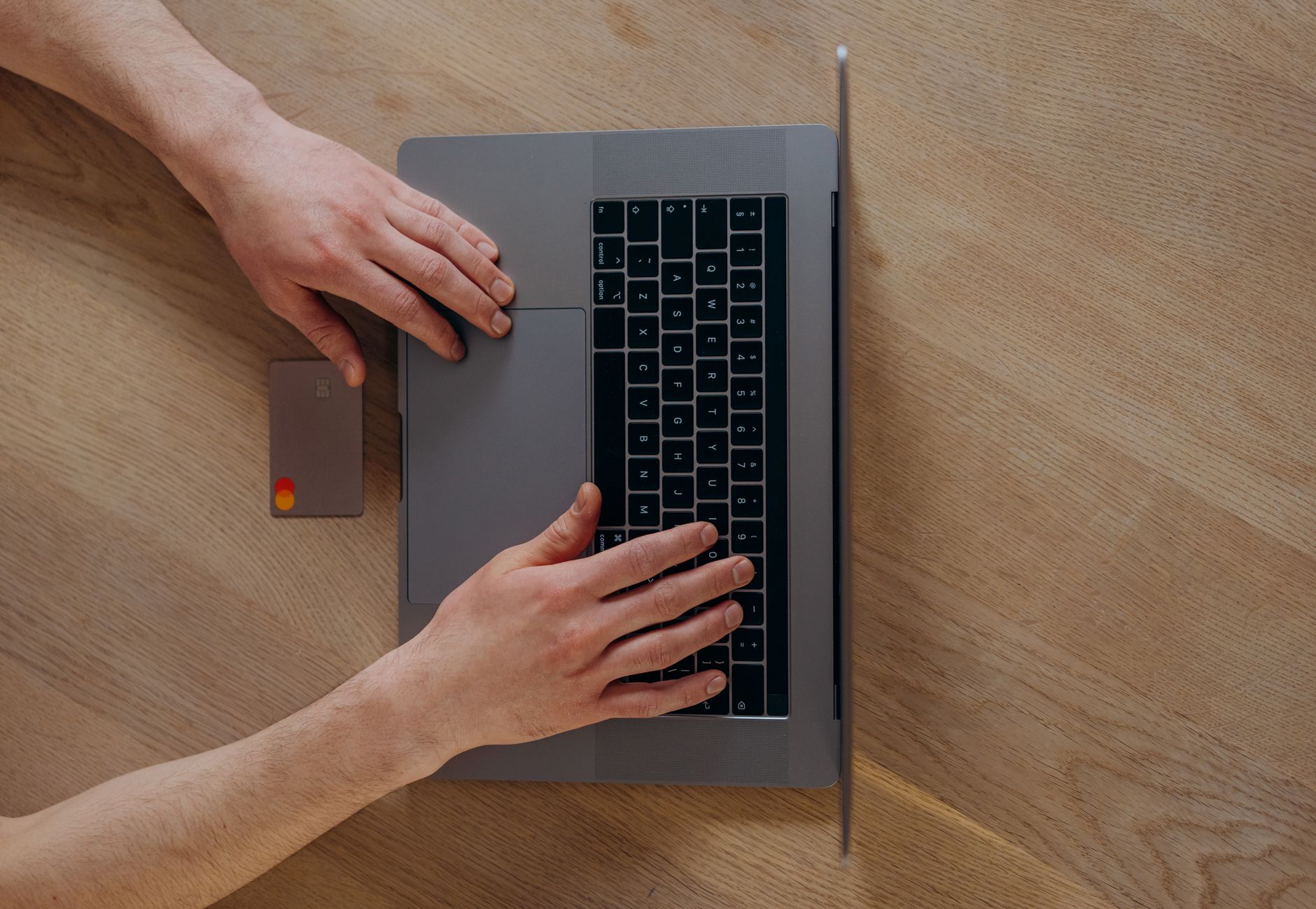 Ręce na laptopie obok karty kredytowej na drewnianym biurku