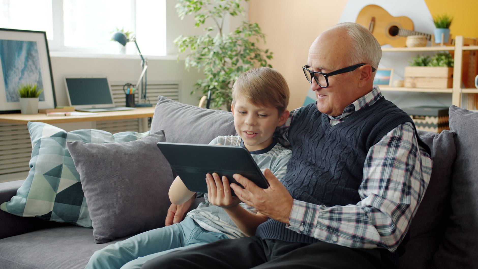 Starszy mężczyzna i chłopiec siedzą na kanapie przeglądając tablet razem